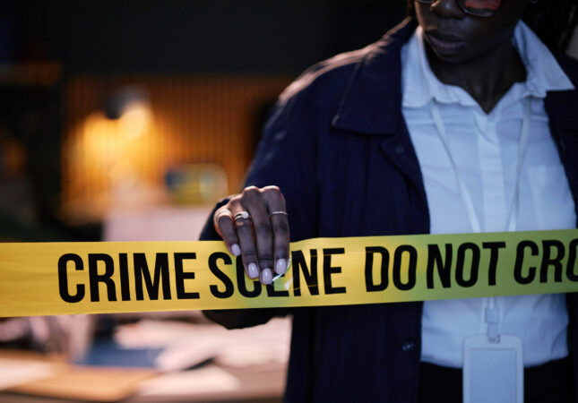 Police officer seen adjusting crime scene tape during a late-night investigation while reviewing evidence on table. Officer wearing professional uniform and badge visible