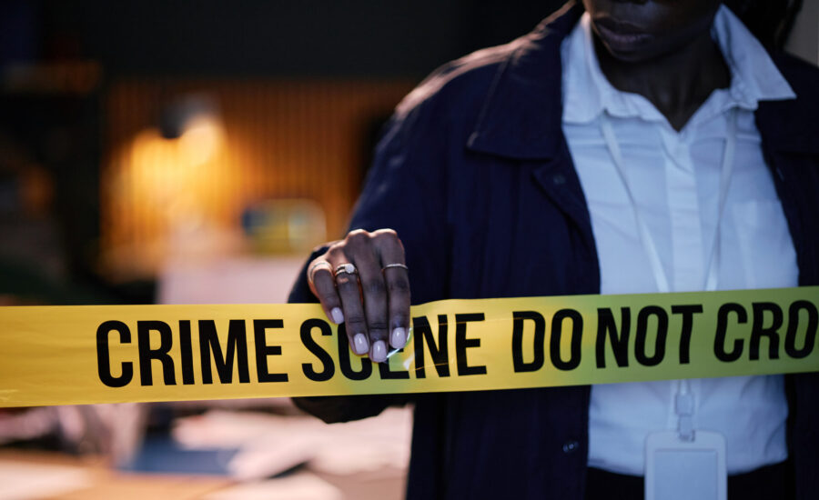 Police officer seen adjusting crime scene tape during a late-night investigation while reviewing evidence on table. Officer wearing professional uniform and badge visible