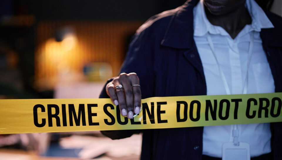Adjusting Crime Scene Tape During Investigation Process Police officer seen adjusting crime scene tape during a late-night investigation while reviewing evidence on table. Officer wearing professional uniform and badge visible